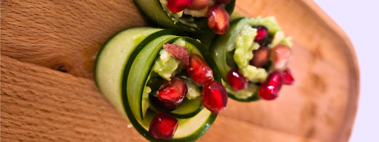 Vegan komkommerrolletjes gevuld met avocado en gegarneerd met granaatappelpitjes op een borrelplank.